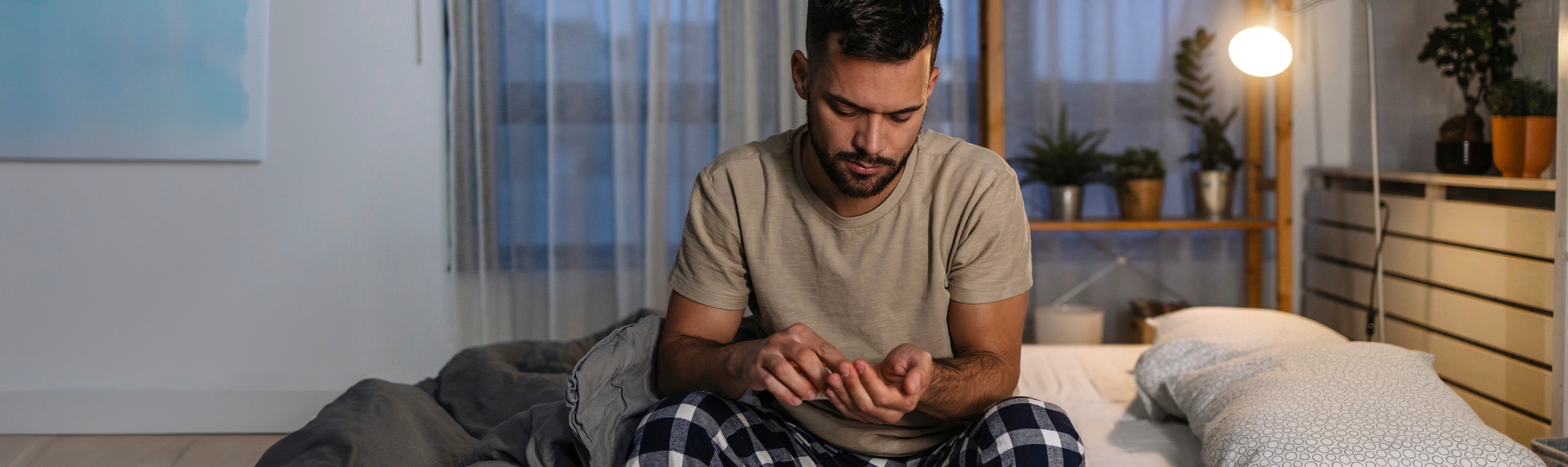 Mann sitzt in der Nacht auf dem Bett und nimmt Schlaftabletten ein