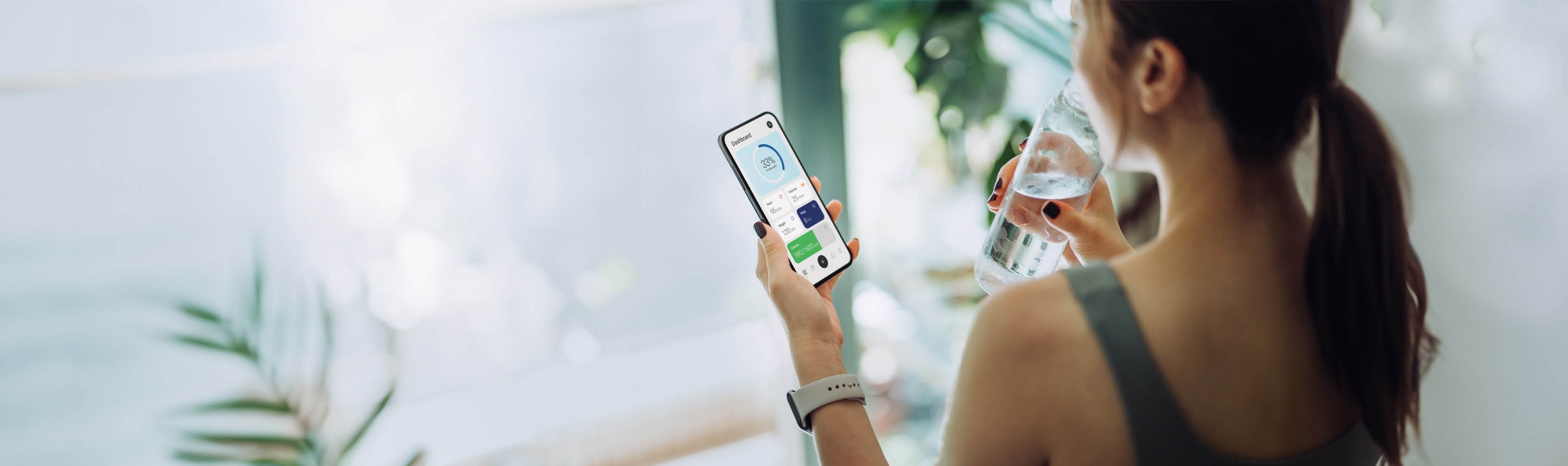 Gesundheits-Apps - Eine sportliche junge Frau schaut auf die Fitness-App auf ihrem Smartphone, während sie aus einer Wasserflasche trinkt.