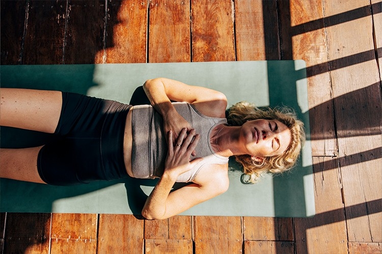 Eine Frau liegt auf einer Yogamatta und versucht, zu entspannen.