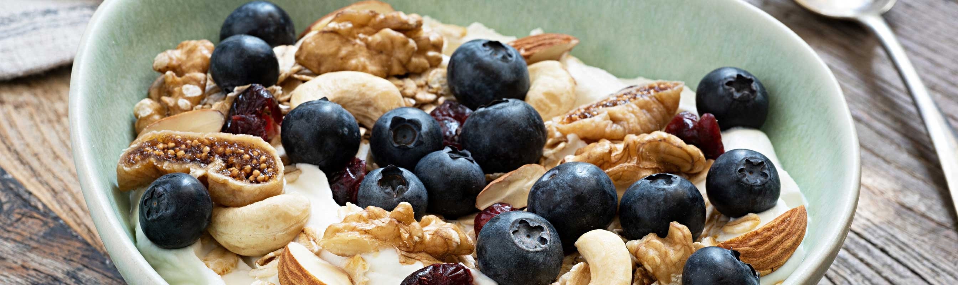 Eine Schale mit Nüssen, Blaubeeren, Haferflocken und Joghurt. 