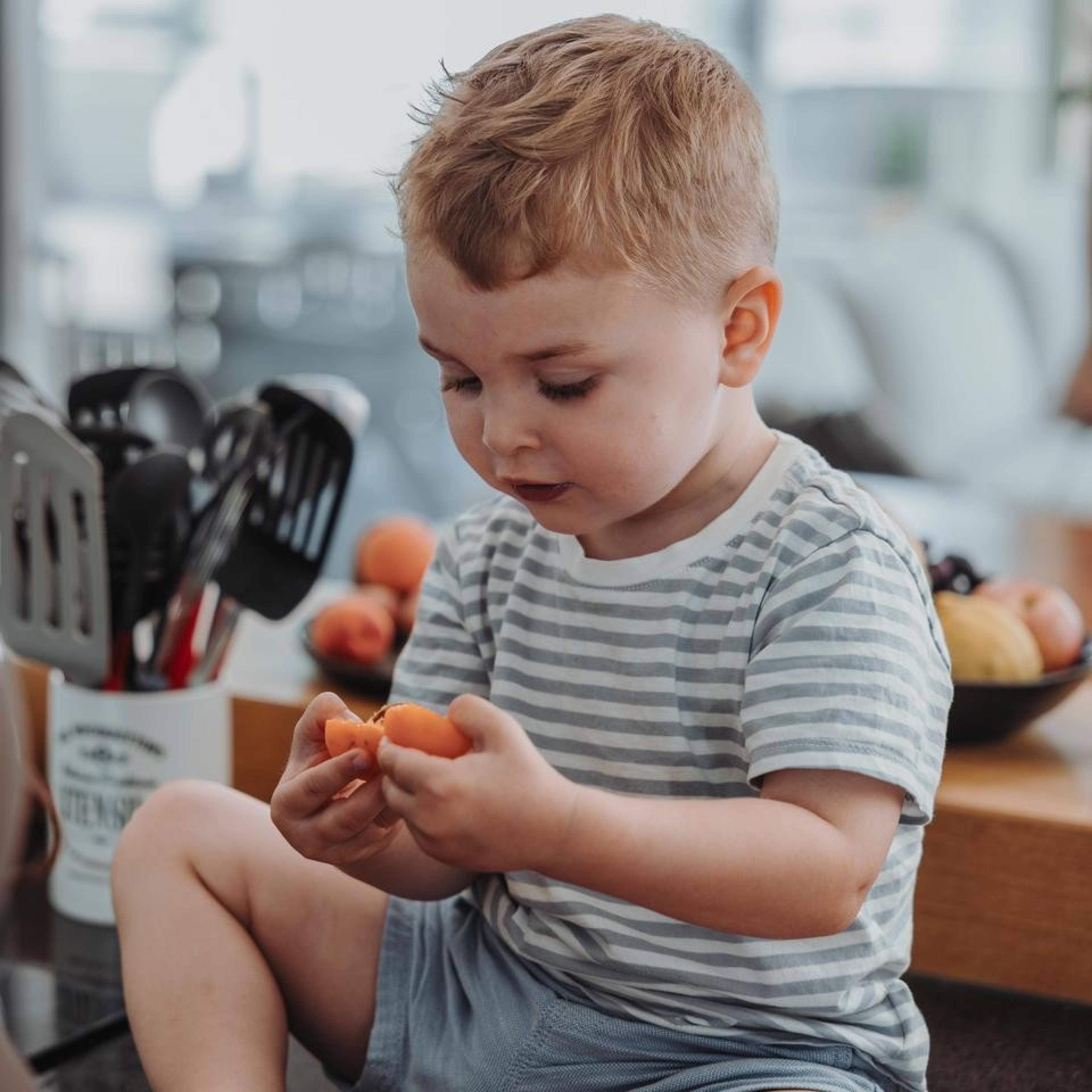 Ein kleiner Junge probiert zum ersten Mal Aprikosen in der Küche