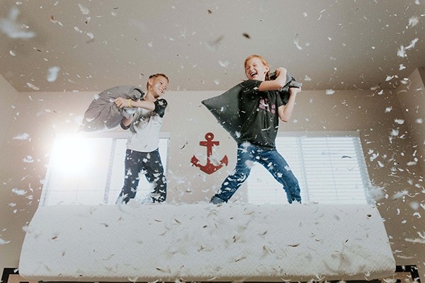 Zwei jungen Buben liefern sich eine Kissenschlacht auf dem Bett