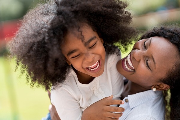 Eine Mutter und ihre Tochter liegen sich lachend in den Armen.
