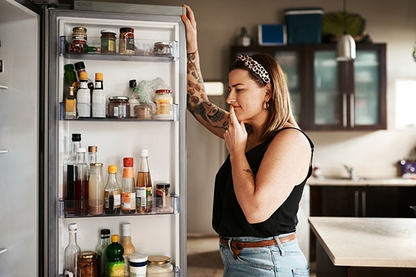 eine junge Frau schaut in den Kühlschrank und kann sich nicht entscheiden was sie essen soll