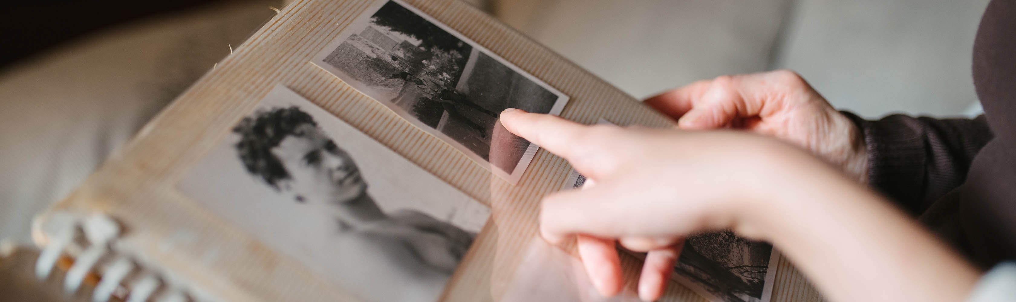 Eine ältere Person schaut sich mit einem Familienmitglied ein altes Fotoalbum an und versucht sich an die Zeit zu erinnern.