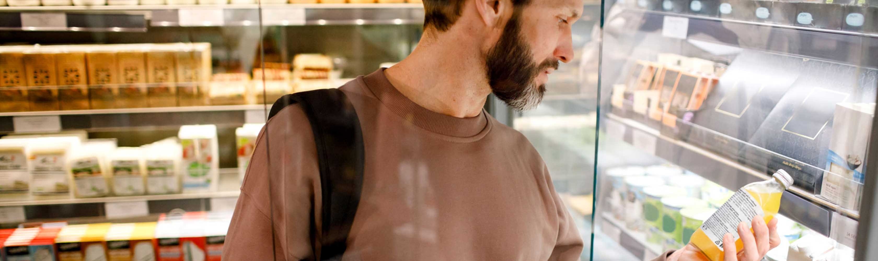 Ein Mann steht vor dem Kühlregal im Supermarkt und liest die Inhaltsstoffe auf einer Flasche Orangensaft.