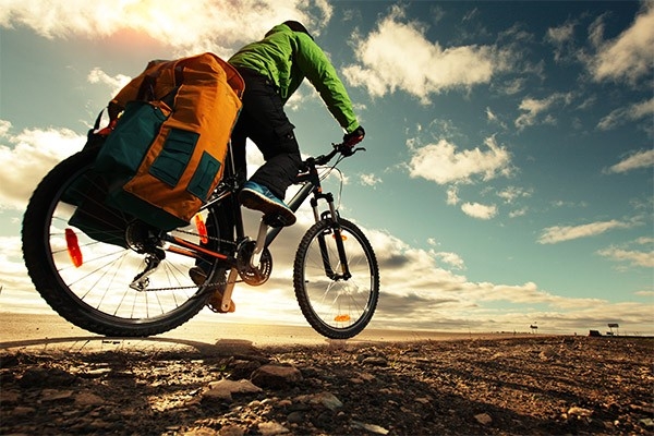 Ein Mann fährt bei Abendstimmung auf einem Velo durch die Landschaft. Zur Vorbereitung einer solchen Reise gehört die medizinische Reiseberatung und eine entsprechend ausgestattete Reiseapotheke.