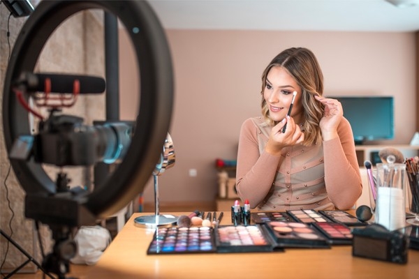 Eine Frau sitzt an einem Schminktisch und nimmt einen Beauty-Vlog auf.