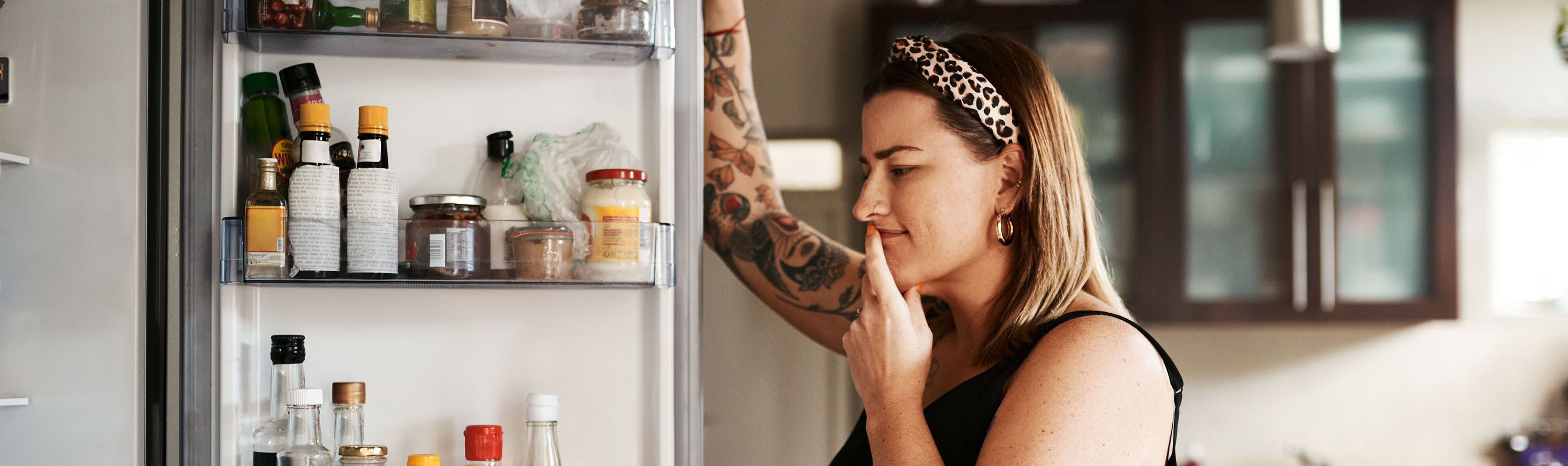 Eine Frau vor dem Kühlschrank fragt sich, wie sie mit Ernährungsumstellung gesünder essen kann..