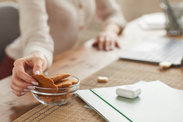 Gesunder Lebensstil im Homeoffice? Eine Frau sitzt am Schreibtisch und greift zur Schale mit den Guetzli. Beim Snacking aufpassen, um die Übersicht nicht zu verlieren, was und vor allem wie viel gegessen wurde.