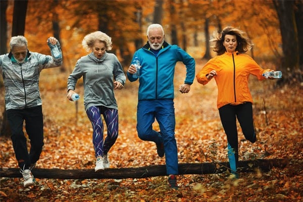 Vorsätze wie ein gesunder Lebensstil erfordern, das Verhalten zu ändern und beim Umsetzen Hürden zu überwinden. Wie diese Laufgruppe, die einen querliegenden Baumstamm im Wald überwindet.