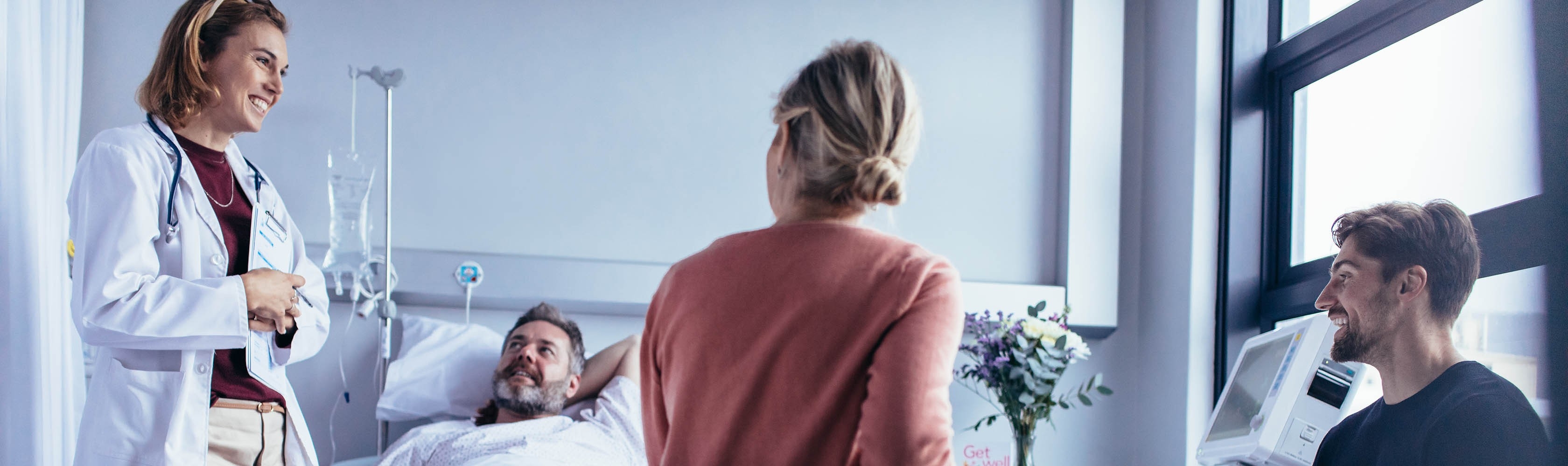 Eine Pflegeperson unterhält sich im Zimmer mit einem Patienten und den Angehörigen