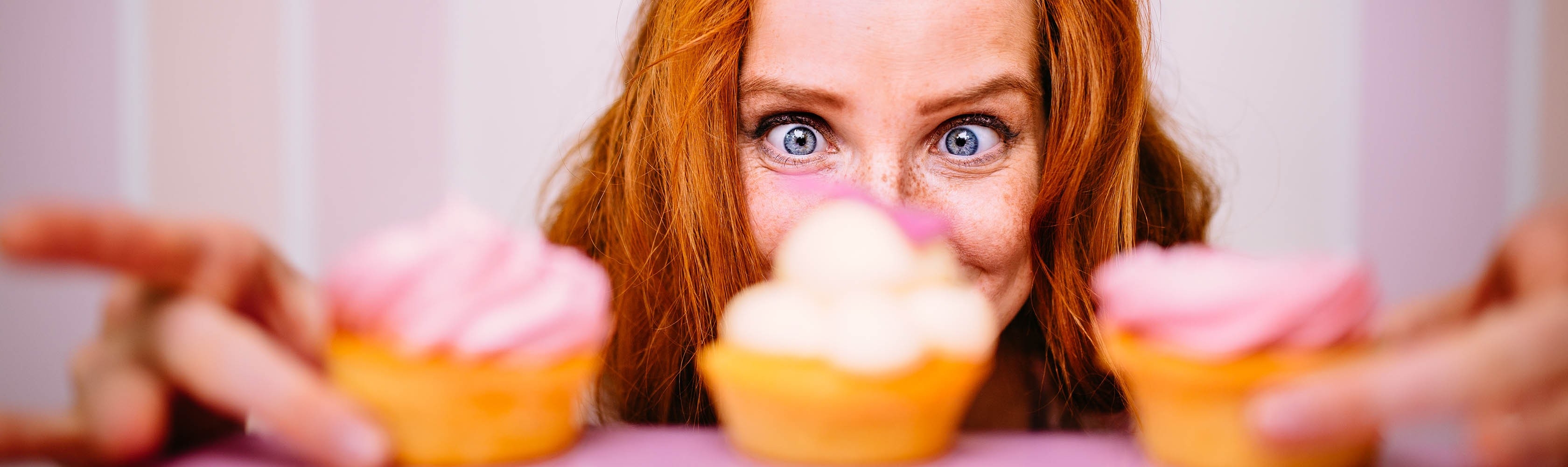 Eine Frau hat drei Cupcakes vor sich und versucht der Lust zu wiederstehen.