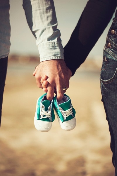 Ein Paar hält gemeinsam Babyschuhe in der Hand. Ihr Kinderwunsch scheint bereits konkret zu sein. Vielleicht sind sie auch schon werdende Eltern.