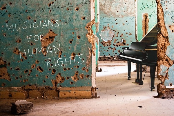 Eine grüne Wand in einem alten Haus zeigt Einschusslöcher und den Schriftzug «Musicians for Human Rights». Im Hintergrund wartet ein schwarzer Flügel auf die Musiker.