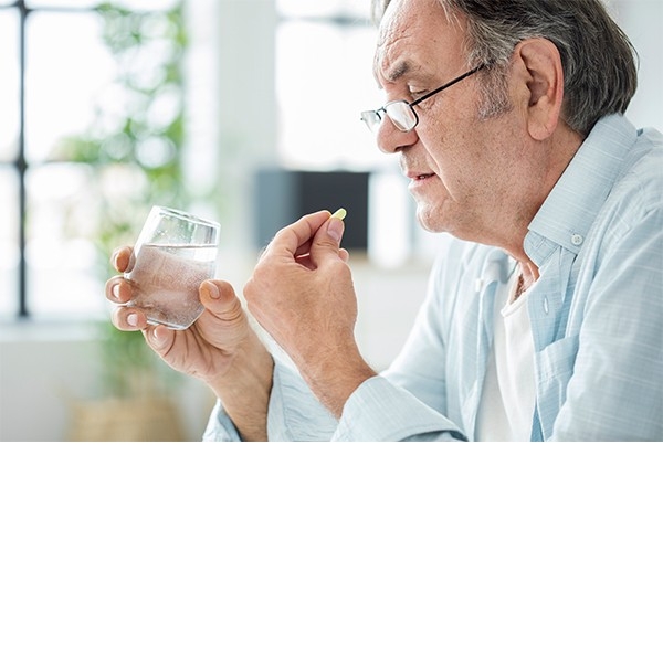 Medikamente richtig einnehmen: Ein Mann hält ein Glas Wasser und eine Tablette in der Hand.