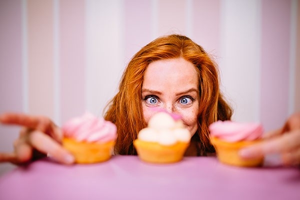 Eine Frau blickt freudig auf drei bunte Cupcakes.