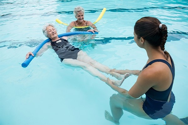 Auch im Alter ist Schwimmen lernen möglich. Zwei ältere Frauen und eine junge Schwimmlehrerin führen Schwimmübungen im Wasser durch.