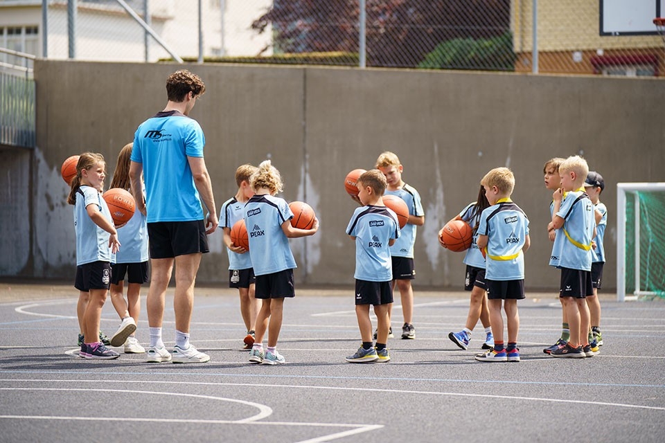 Kinder stehen mit Basketballbällen mit dem Trainer im Kreis
