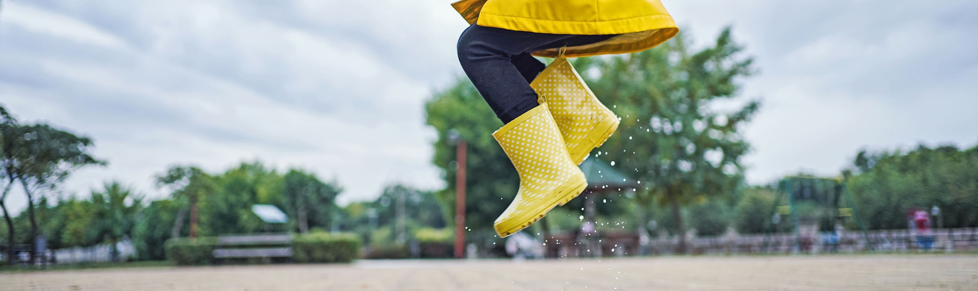 Ein Kind hüpft begeistert in eine Regenpfütze – komplett stressfrei und unbeschwert.