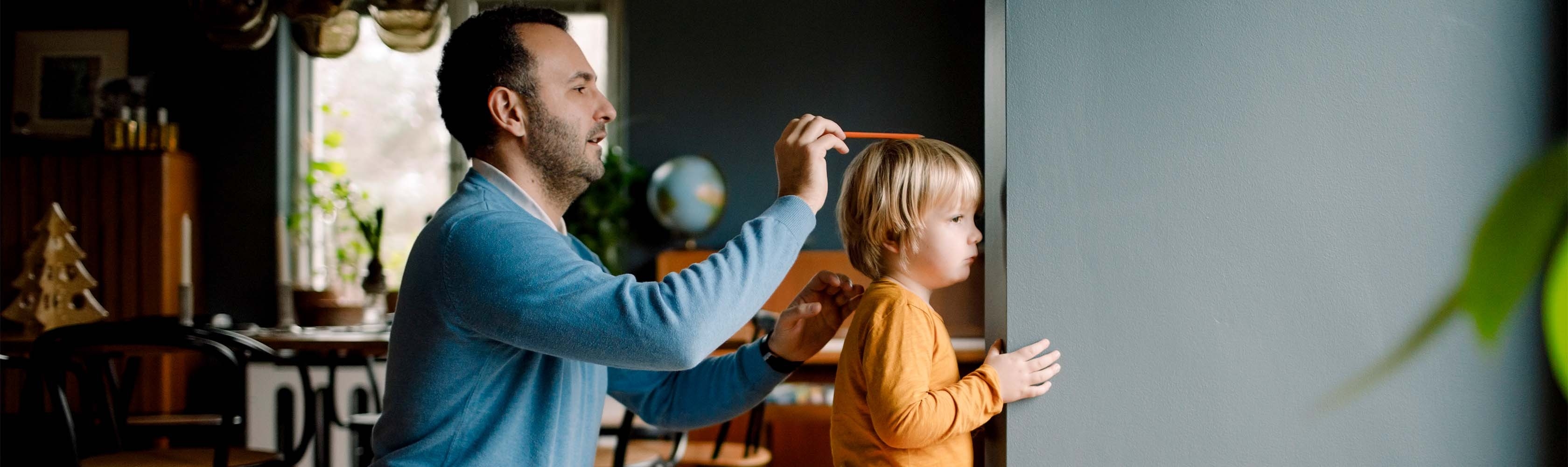 Vater misst die Grösse des Kindes mit einem Bleistift an der Wand.