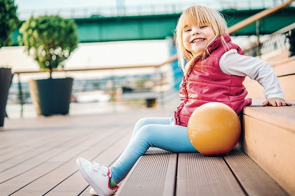 Ein kleines Kind sitzt auf einer Treppe und lächelt strahlend in die Kamera. Eine Zahnversicherung lohnt sich, besonders für Kinder.